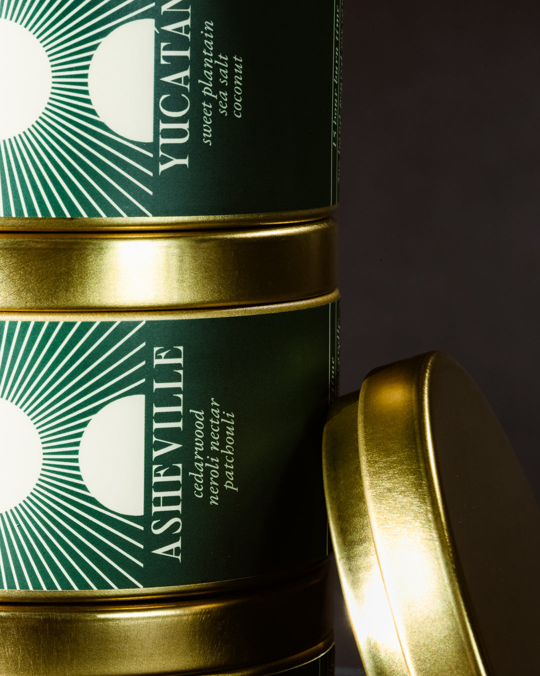Two green tins with gold lids labeled 'Yucatan' and 'Asheville' on a dark background.
