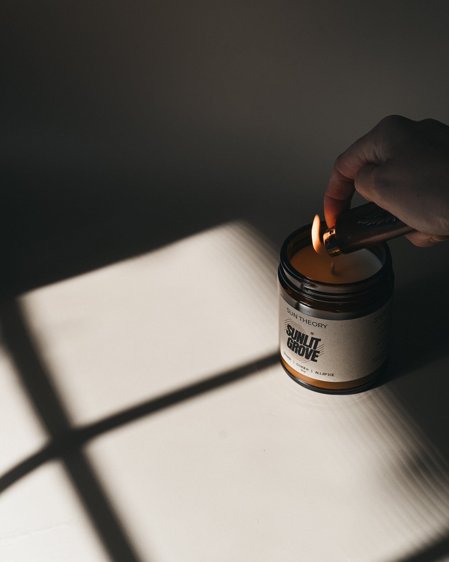 Hand lighting a candle labeled 'Sunlit Grove' with a dark background