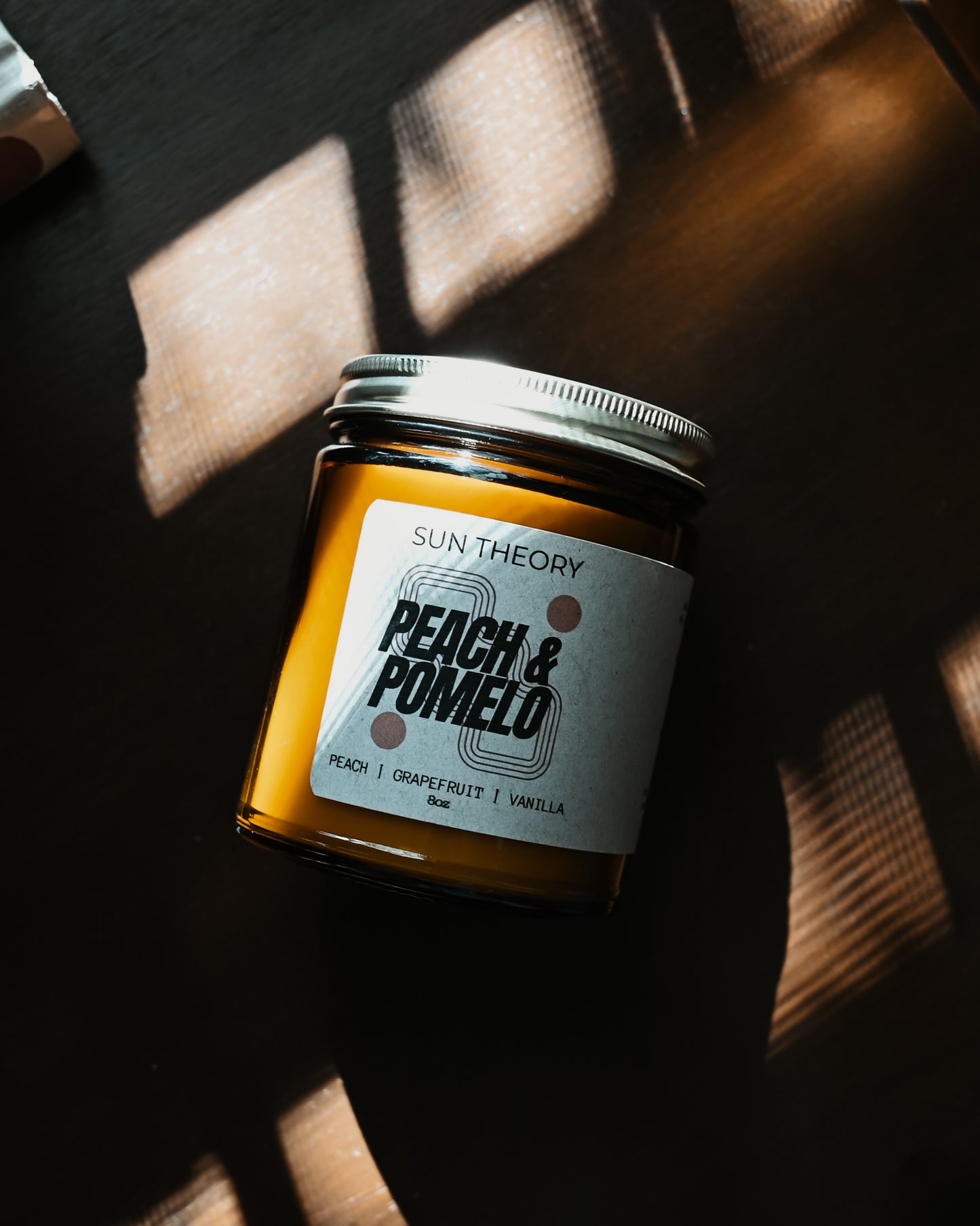 Jar of 'Peach & Pomelo' candle by Sun Theory on a dark surface with light shadows.