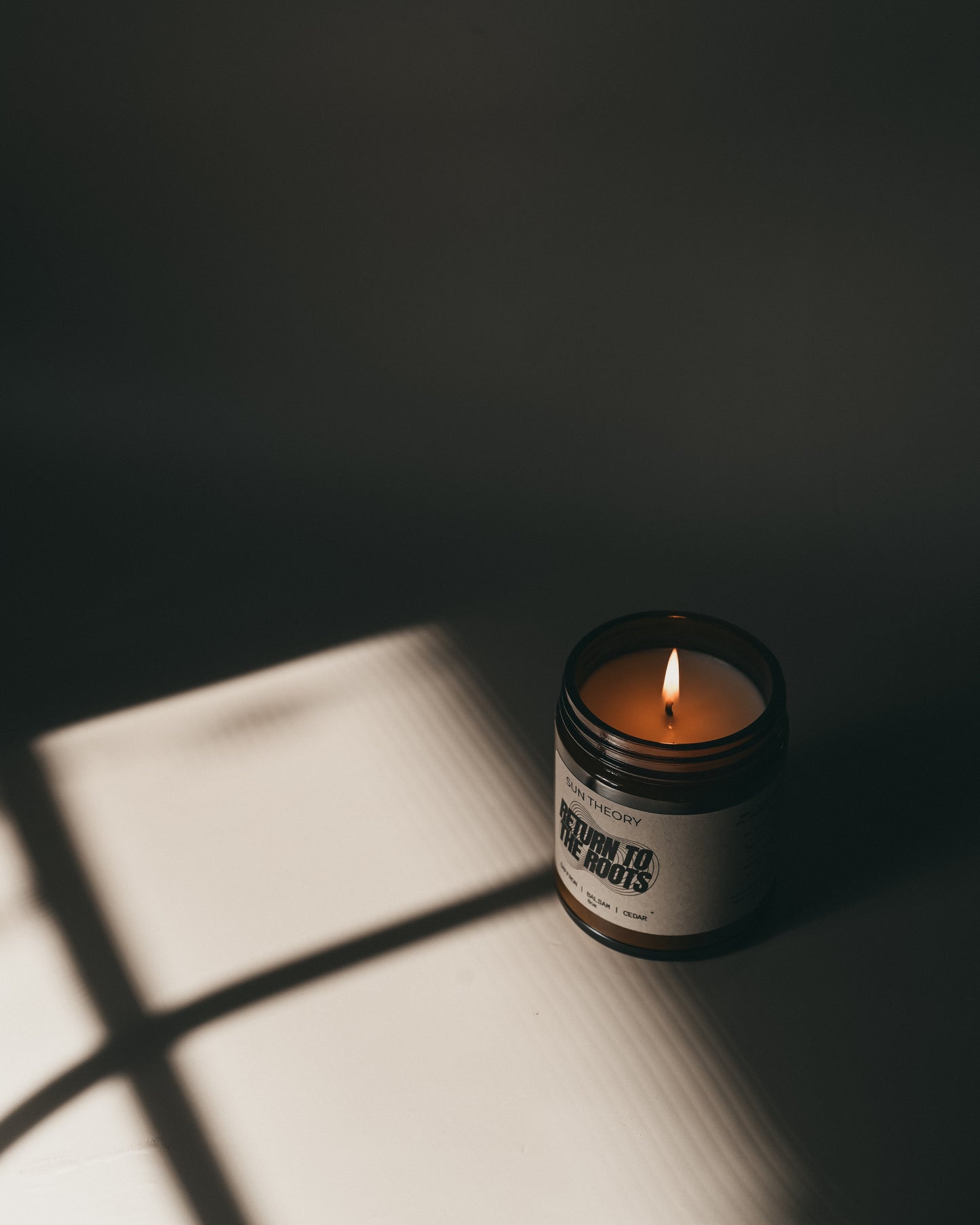 Candle in a jar labeled 'Return to the Roots' casting a shadow on a surface.