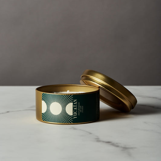 Candle in a green tin with a gold lid on a marble surface