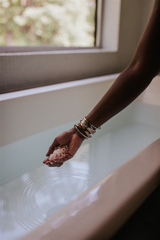 Hand holding a bath soak over a bathtub with a blurred window in the background