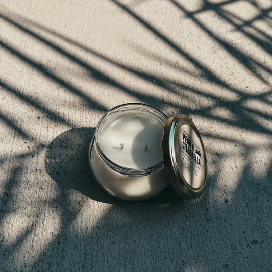 Candle in a glass jar with a metal lid on a textured surface with shadow patterns