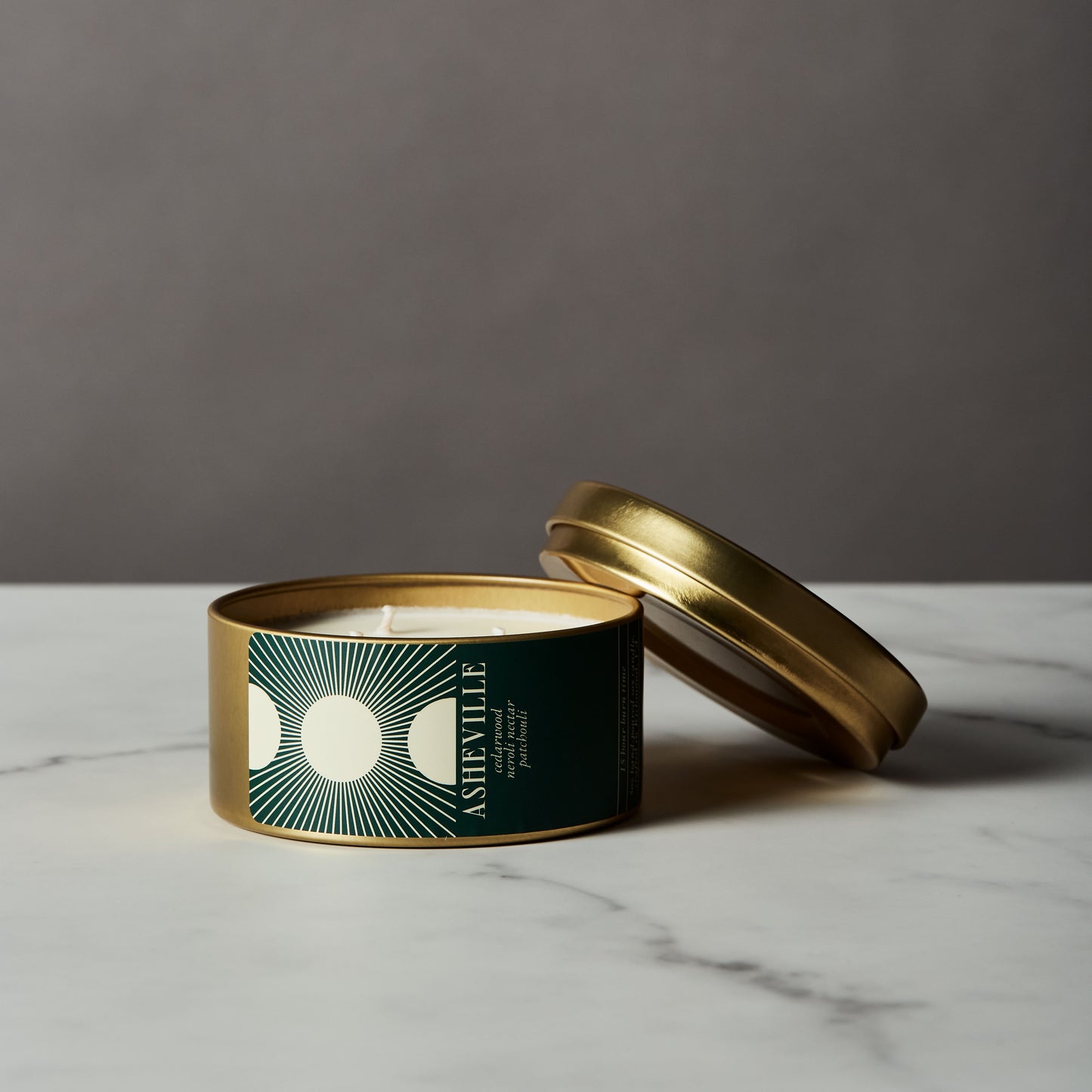 Asheville candle in a gold tin with a green label on a marble surface