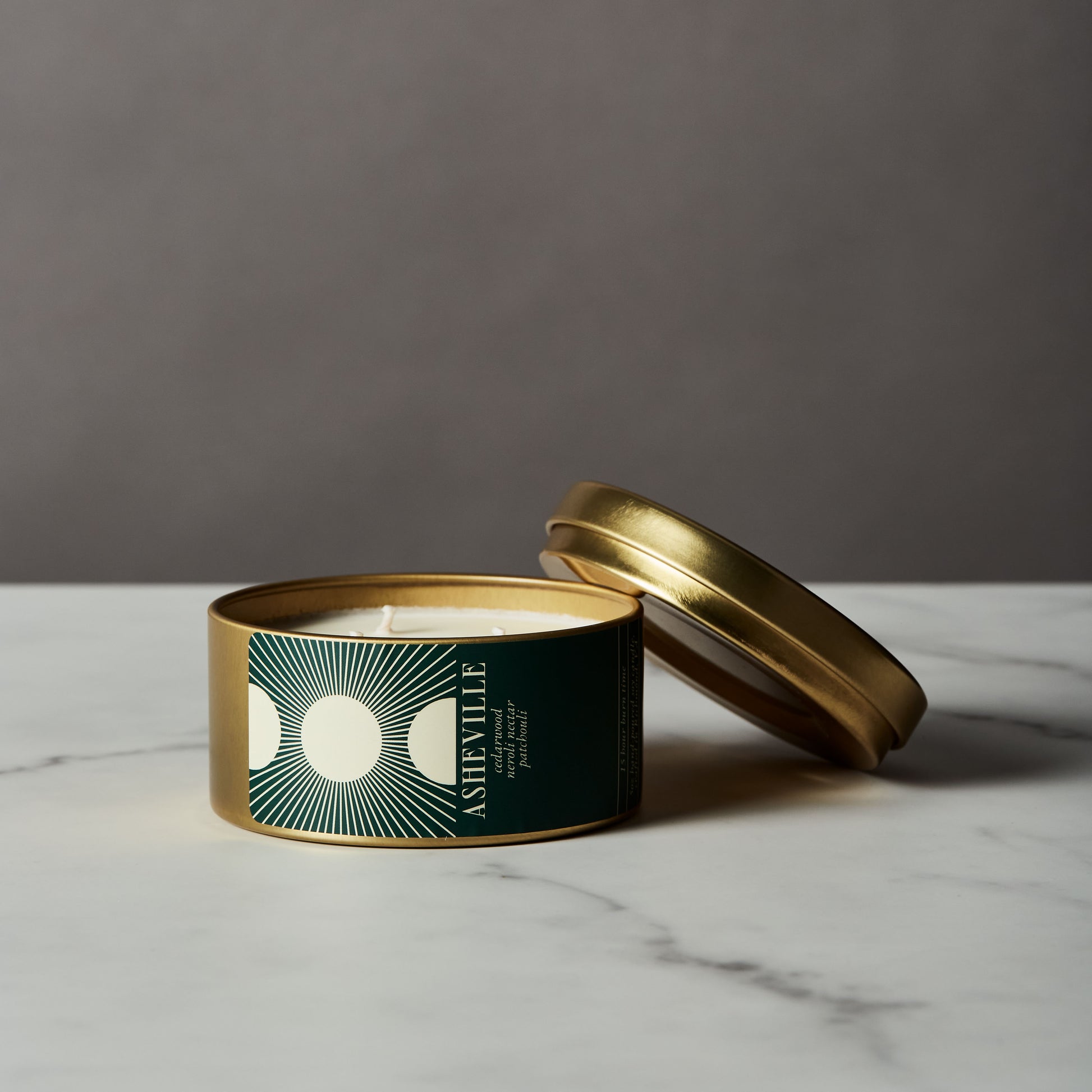 Asheville candle in a gold tin with a green label on a marble surface