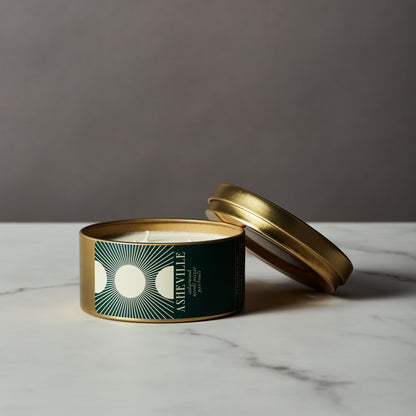 Asheville candle in a gold tin with a green label on a marble surface