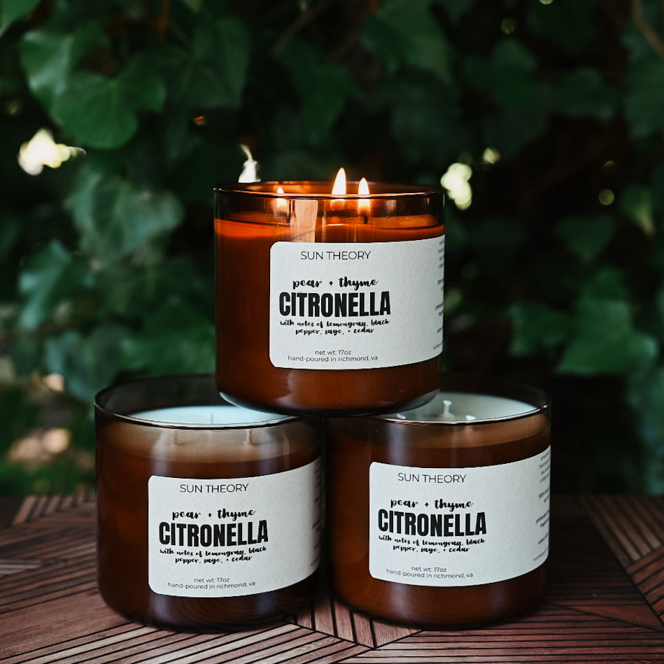 Three brown glass candles in a sun theory branded amber glass jar, with labels reading 'Citronella' and various other product details.
