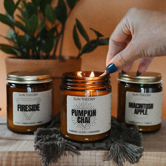 Trio of fall candle jars being lit by a hand focused on a Pumpkin Chai candle
