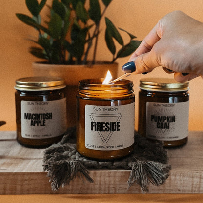 Trio of fall candle jars being lit by a hand focused on a Fireside candle