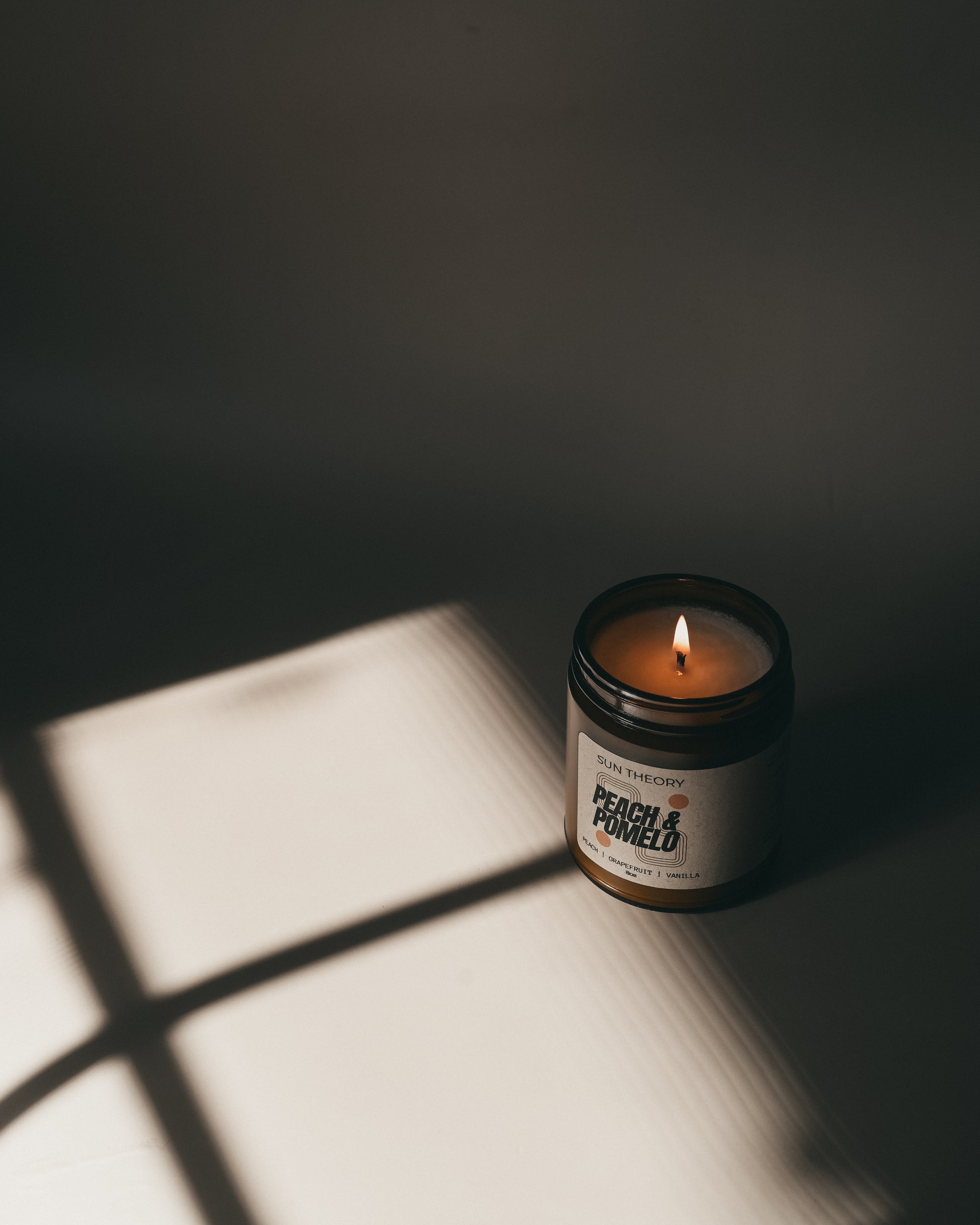 Candle in a jar labeled 'Peach & Powder' casting a shadow on a surface.