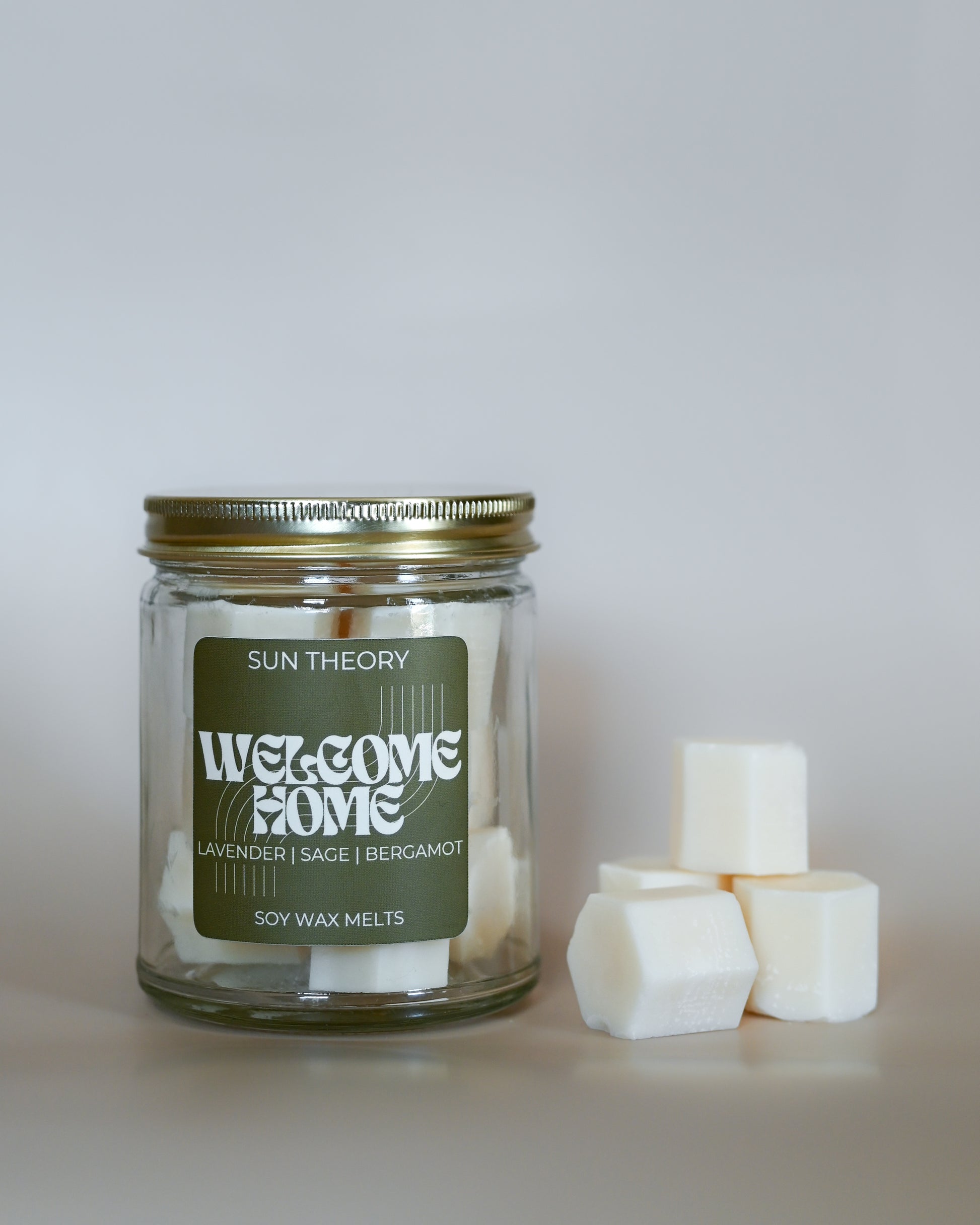 Jar of 'Welcome Home' soy wax melts by Sun Theory with wax melts beside it on a light background