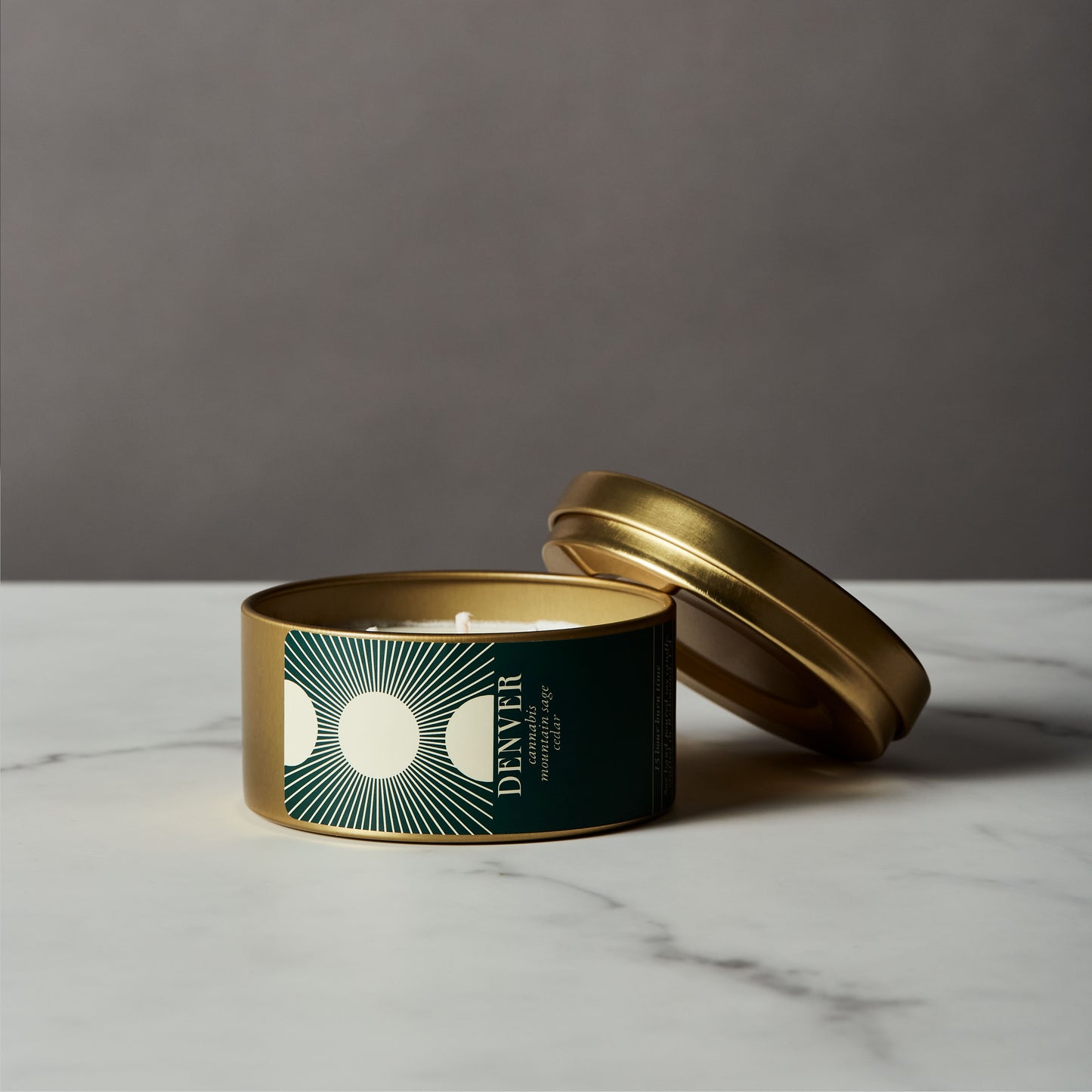 Candle in a decorative tin with a gold lid on a marble surface