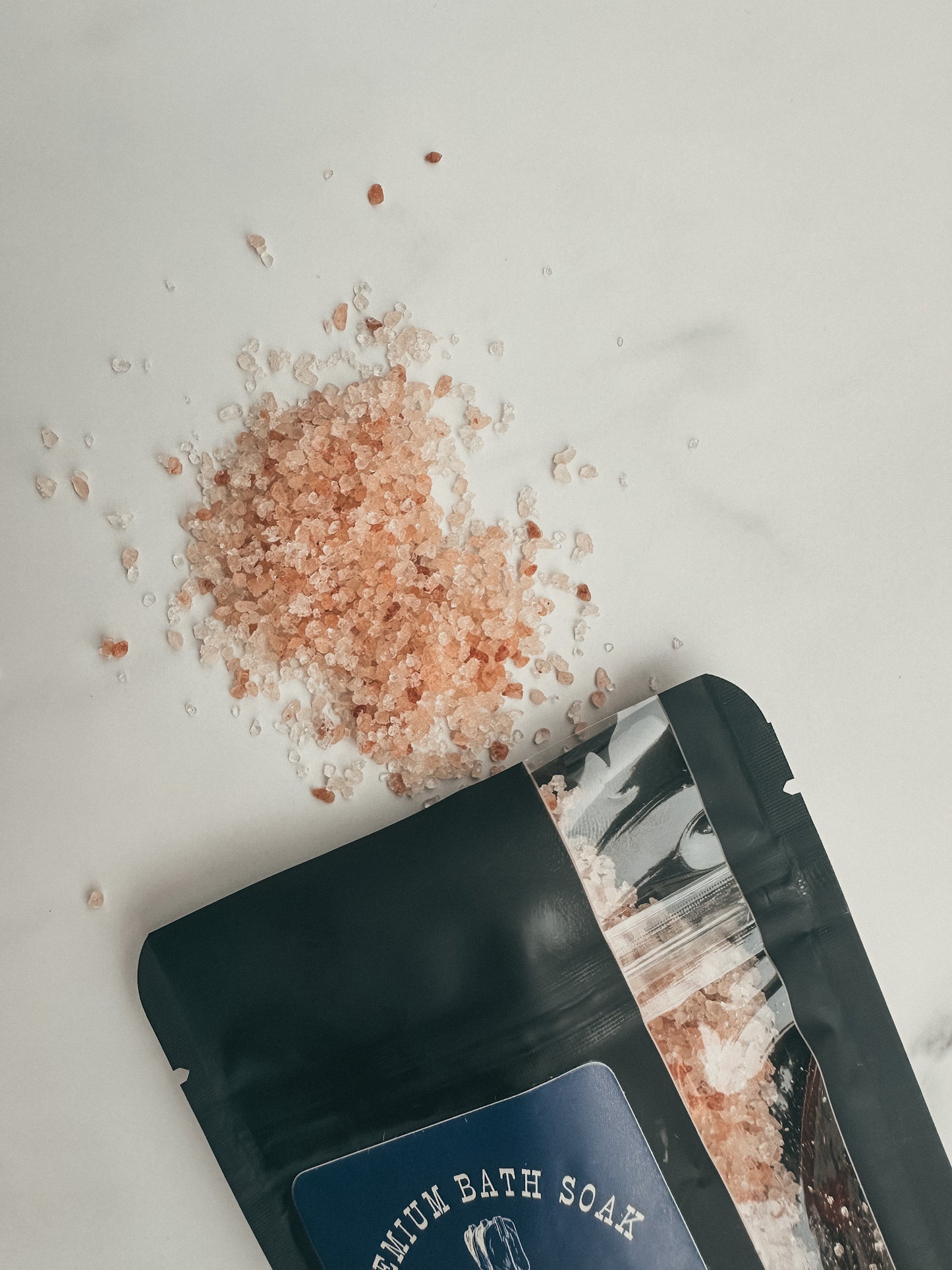Open black packaging of premium bath soak with pink Himalayan salt on a white background