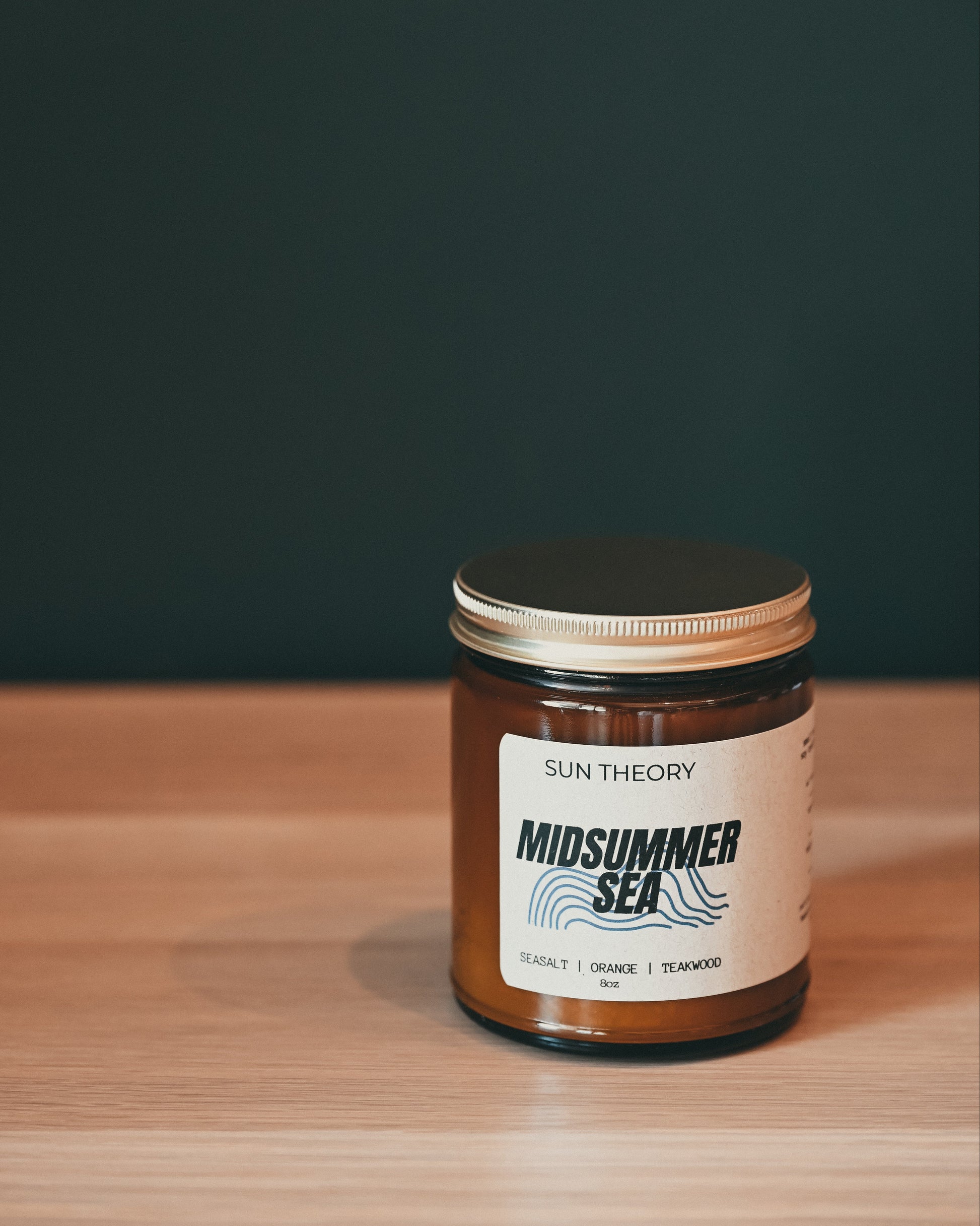 Jar of 'Midsummer Sea' candle by Sun Theory on a wooden surface with a dark background