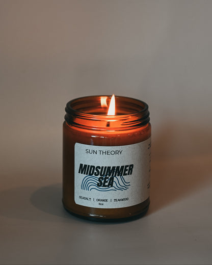 Candle in an amber jar labeled 'Sun Theory Midsummer Sea' on a neutral background