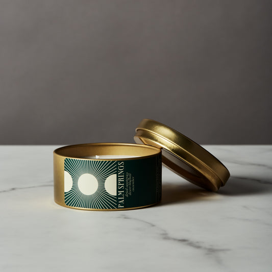 Candle in a gold tin with a green label on a marble surface