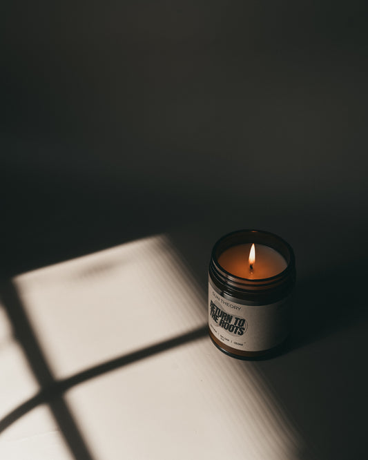Candle in a jar labeled 'Return to the Roots' casting a shadow on a surface.