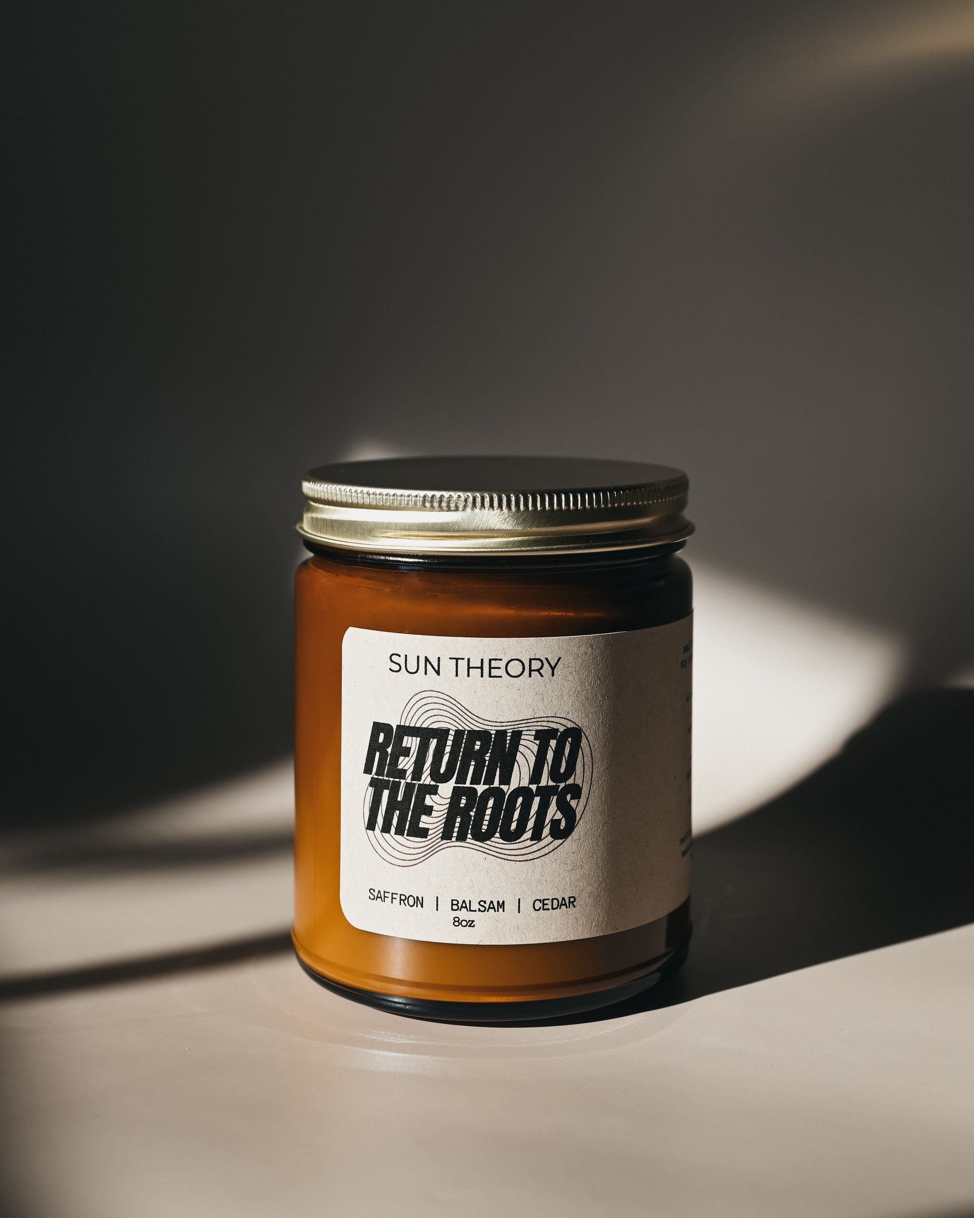 Jar of candle labeled 'Return to the Roots' by Sun Theory on a dark background