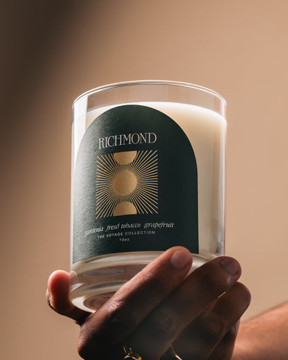 Hand holding a Richmond candle with a dark label against a warm background