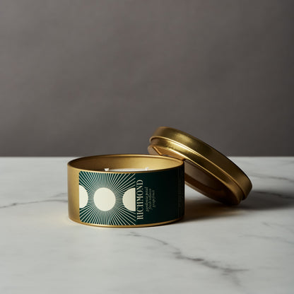 Candle in a gold tin with a green label on a marble surface