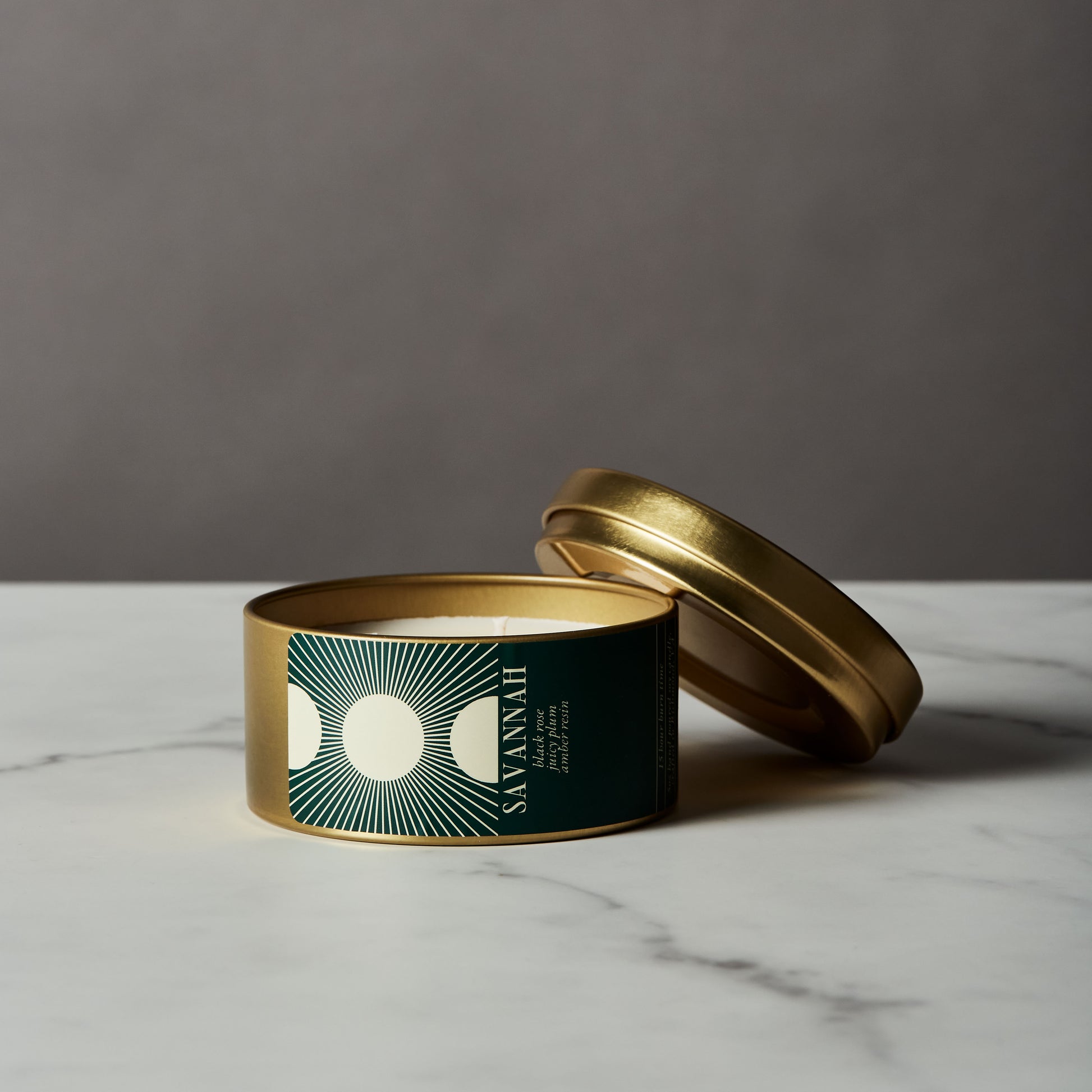 Candle in a gold tin with a green label on a marble surface