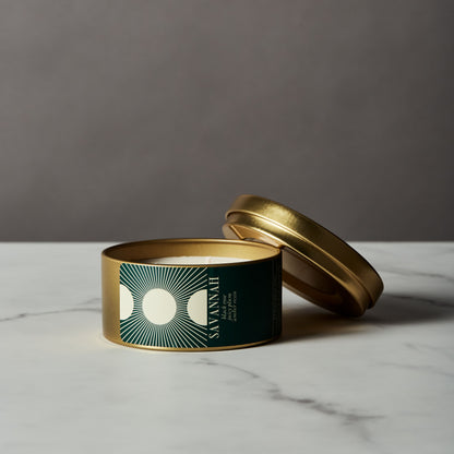 Candle in a gold tin with a green label on a marble surface