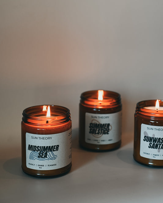Three lit candles in brown jars with labels on a neutral background