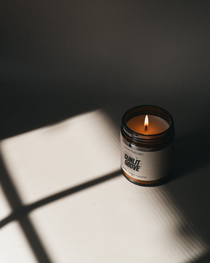 Candle in a jar labeled 'Sunlit Grove' casting shadows on a surface