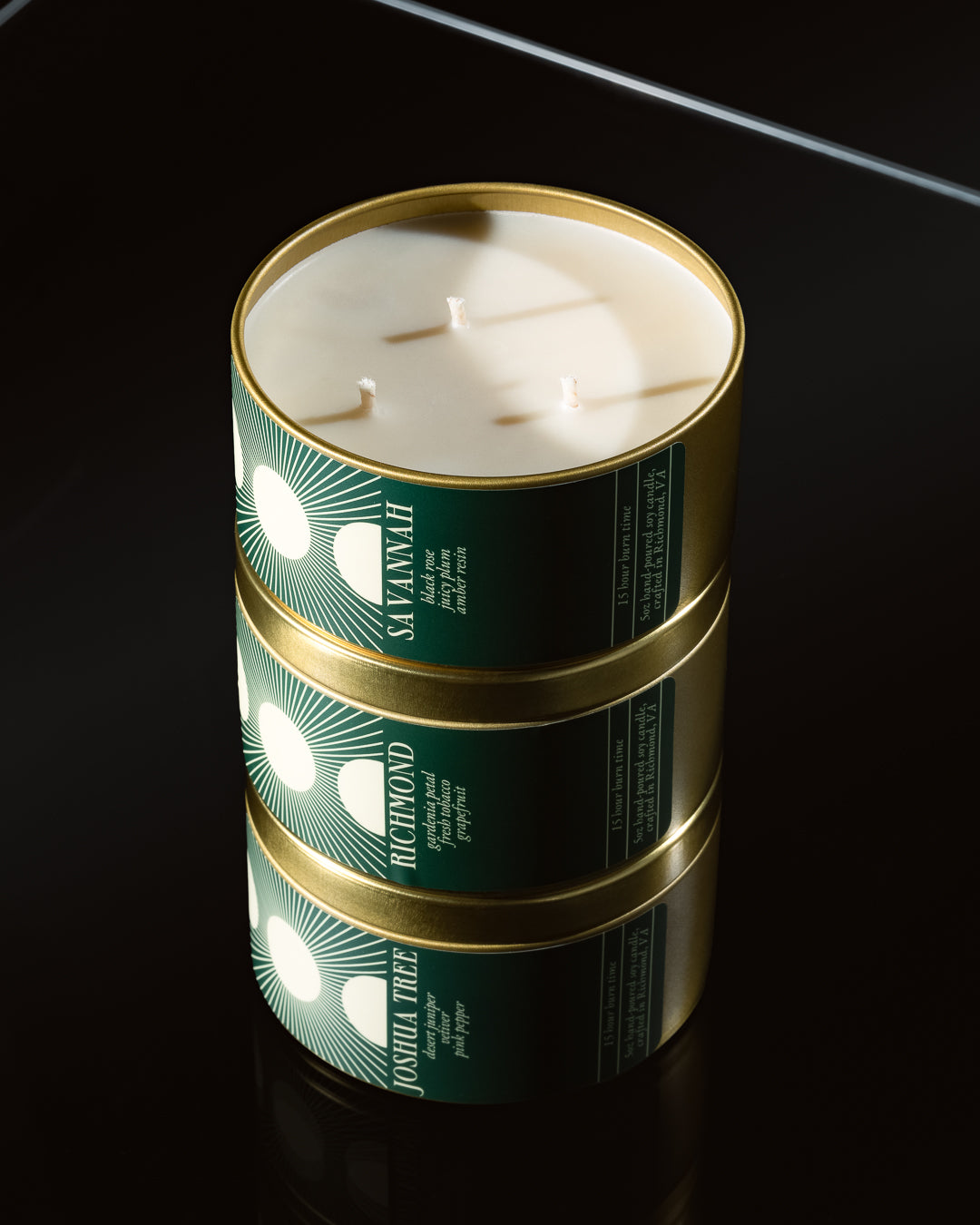 Three stacked candles in green tins with gold lids on a black background
