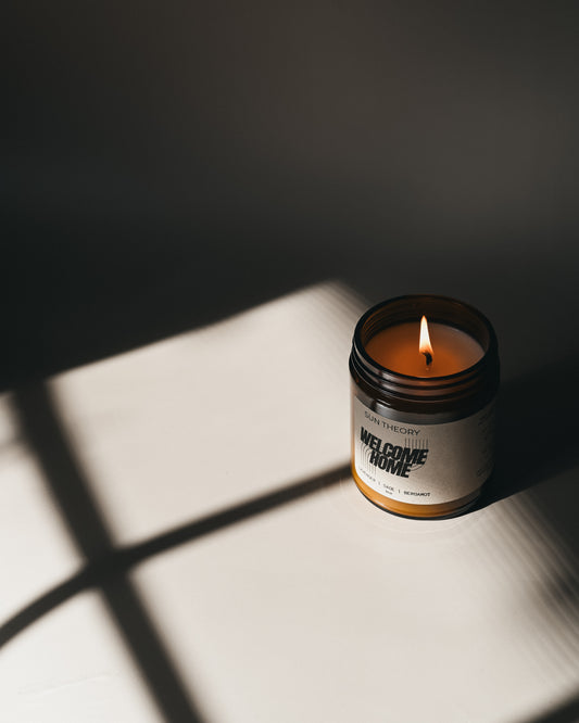 Candle in a jar labeled 'Welcome Home' casting a shadow on a surface.