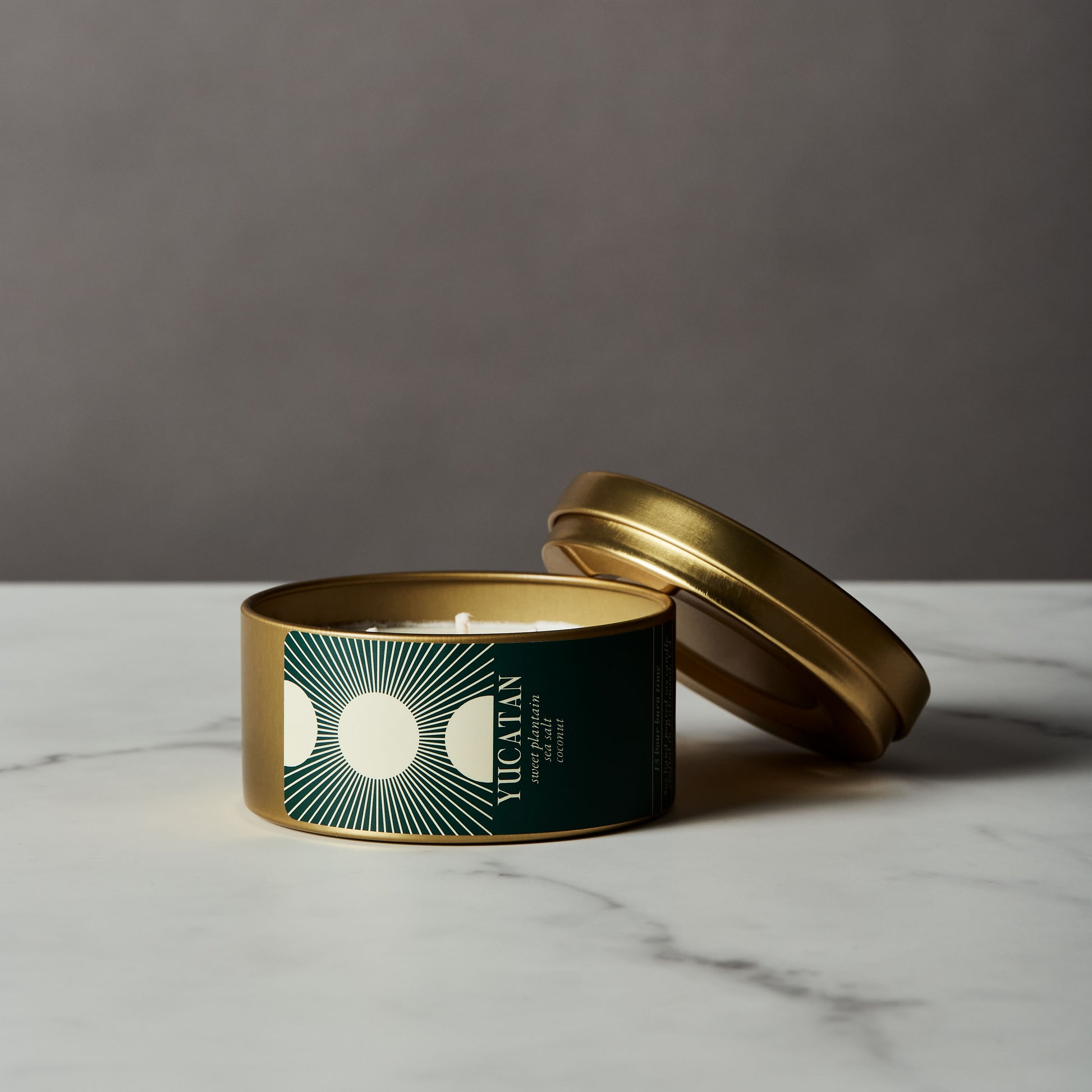 Candle in a green tin with a gold lid on a marble surface