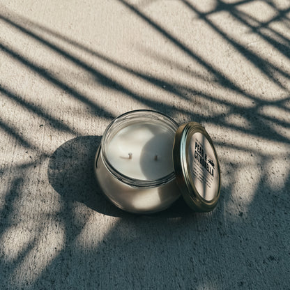 Candle in a glass jar with a metal lid on a textured surface with shadow patterns