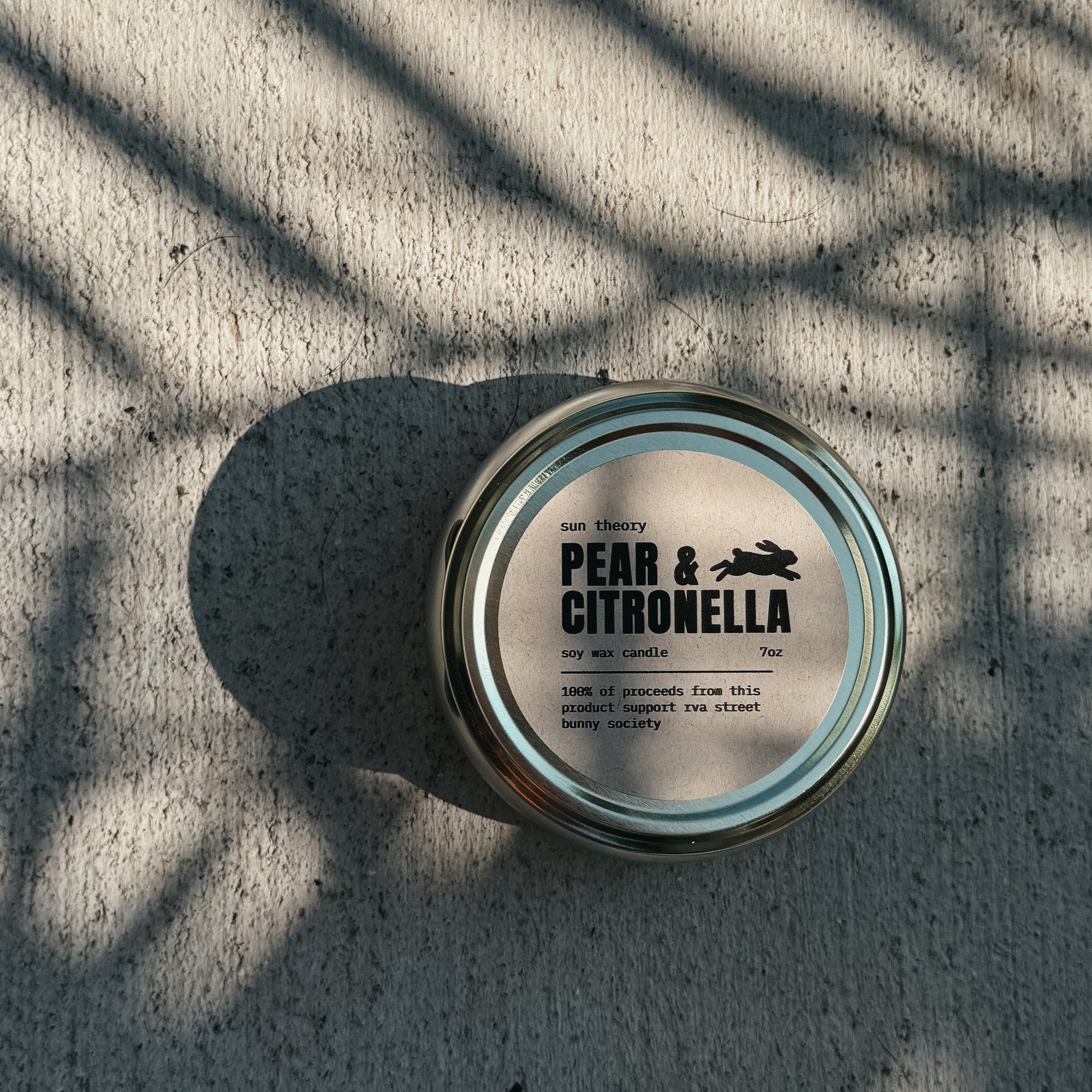 Candle jar labeled 'Pear & Citronella' on a textured surface with shadows.