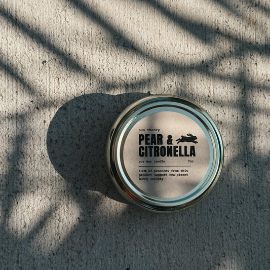 Candle jar labeled 'Pear & Citronella' on a textured surface with shadows.