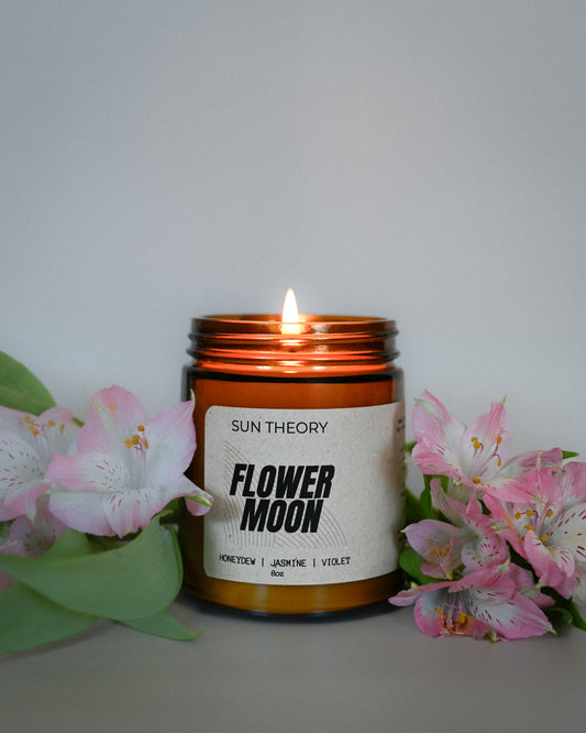 Candle labeled 'Flower Moon' by Sun Theory with flowers on a white background
