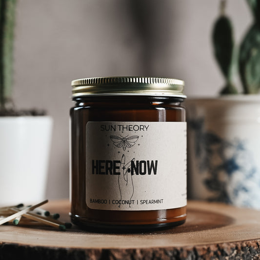 Candle in an amber colored jar labeled "here and now"